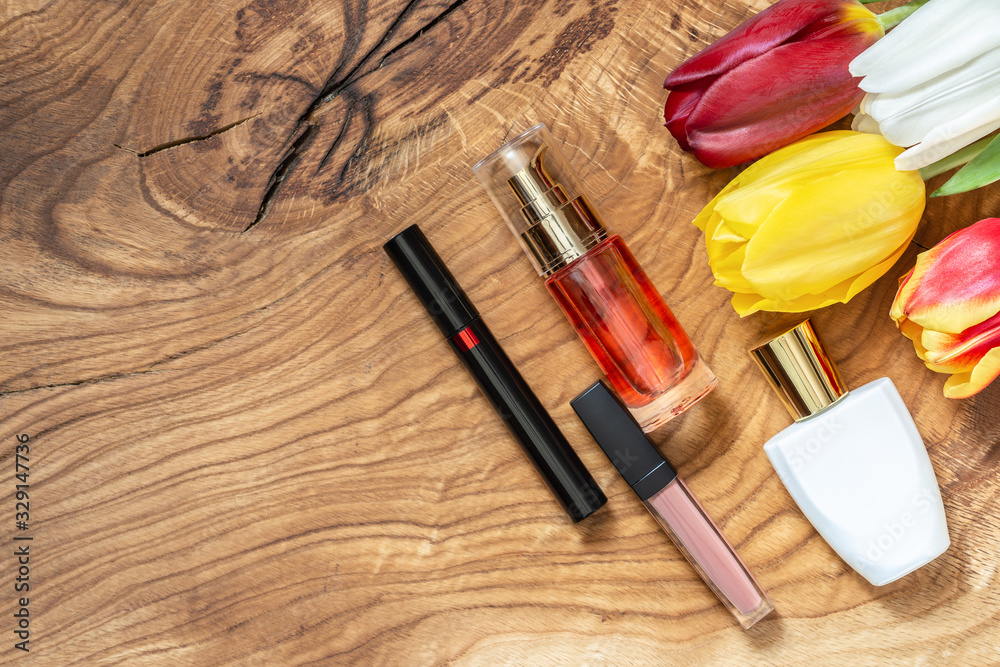 Lipstick, mascara, lotion, perfume, and a bouquet of tulips lie on a wooden table. Spring makeup