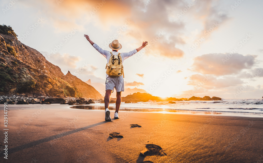 Plakat Young man arms outstretched by the sea at sunrise enjoying freedom and life, people travel wellbeing concept