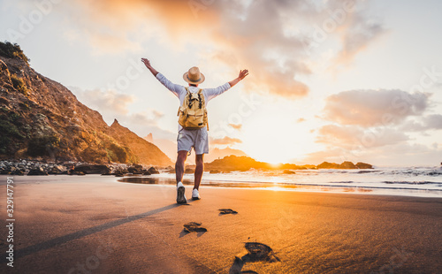 Young man arms outstretched by the sea at sunrise enjoying freedom and life, people travel wellbeing concept	