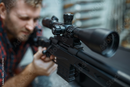 Man checks optical sight on sniper rifle, gun shop