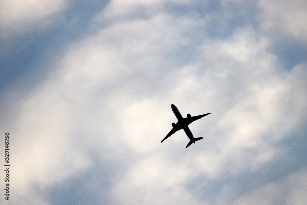 Airplane flying in the blue sky on background of white clouds. Silhouette of a commercial plane during the climb, travel and turbulence concept
