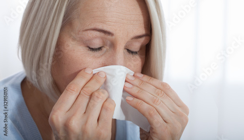 Healthcare, cold, allergy and people concept, sick woman blowing her runny nose in paper tissue on white background