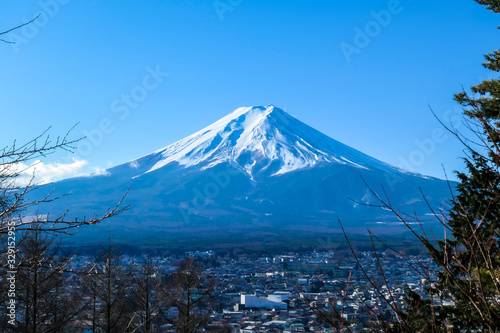A distant view on Mt Fuji in Japan through the pine trees' branches, captured on a clear, wintery day. The top parts of the volcano are covered with a layer of snow. Holly mountain. Mystery and beauty