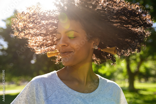 Photography Smiling woman twirling her curly hair outside in a park
