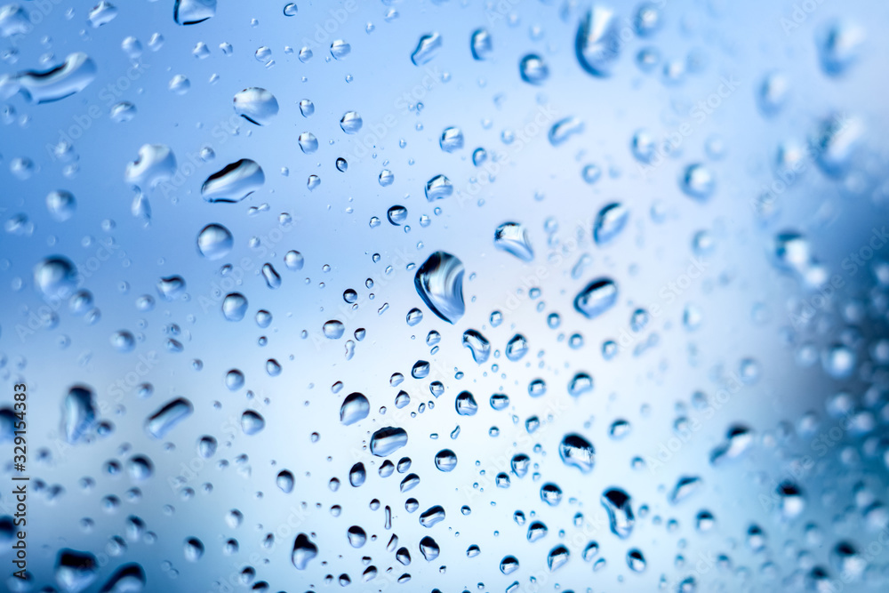 Wet glass with raindrops closeup on blue sky background_