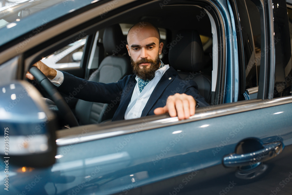 Smiling man poses in automobile, car dealership