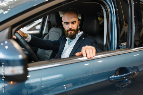 Smiling man poses in automobile, car dealership