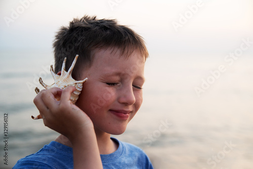 A blind boy listens to the sound of the sea, leaning a seashell against his ear.