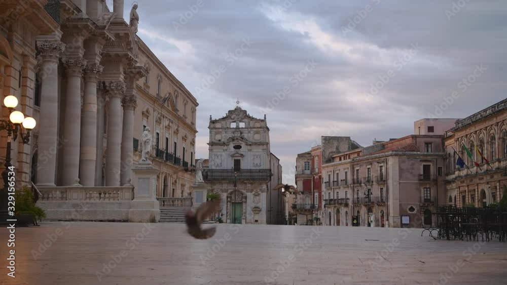 Pigeons (close view) flying over the empty main square Of Syracuse, its old part Ortygia island in Sicily at cloudy sunrise 
