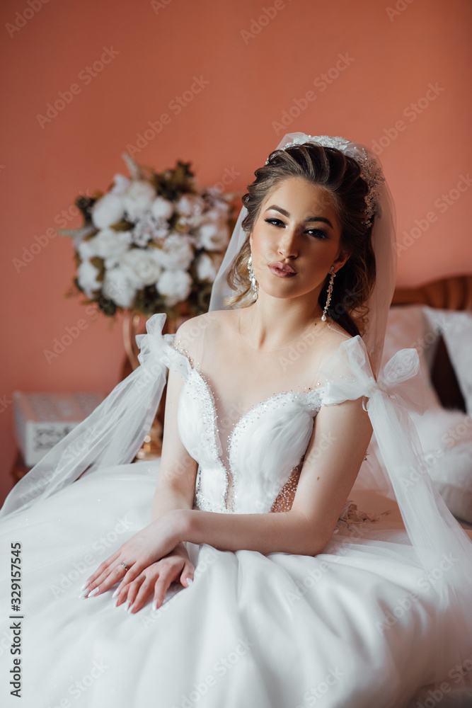 Pretty young girl in white dress at home with veil. Bride with luxurious hair and makeup. Wedding. Preparing the bride for the upcoming wedding. Sexy bride. Bride's fees. Bride morning preparation. Pretty young girl in white dress at home with veil. Bride with luxurious hair and makeup. Wedding. Preparing the bride for the upcoming wedding. Sexy bride. Bride's fees. Bride morning preparation.