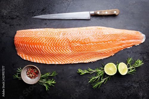 Fresh raw salmon or trout sea fish fillet with spices and herbs on black background, top view