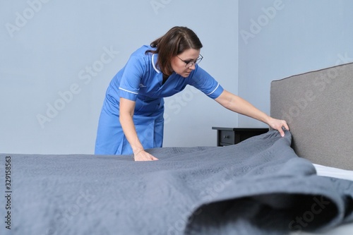 Cleaning service in hotel room, woman maid preparing guest room making bed