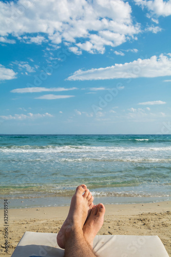 Holiday concept. Man feet close-up relaxing on beach, enjoying the sun.  Enjoying sun lounger on sunny summer day.