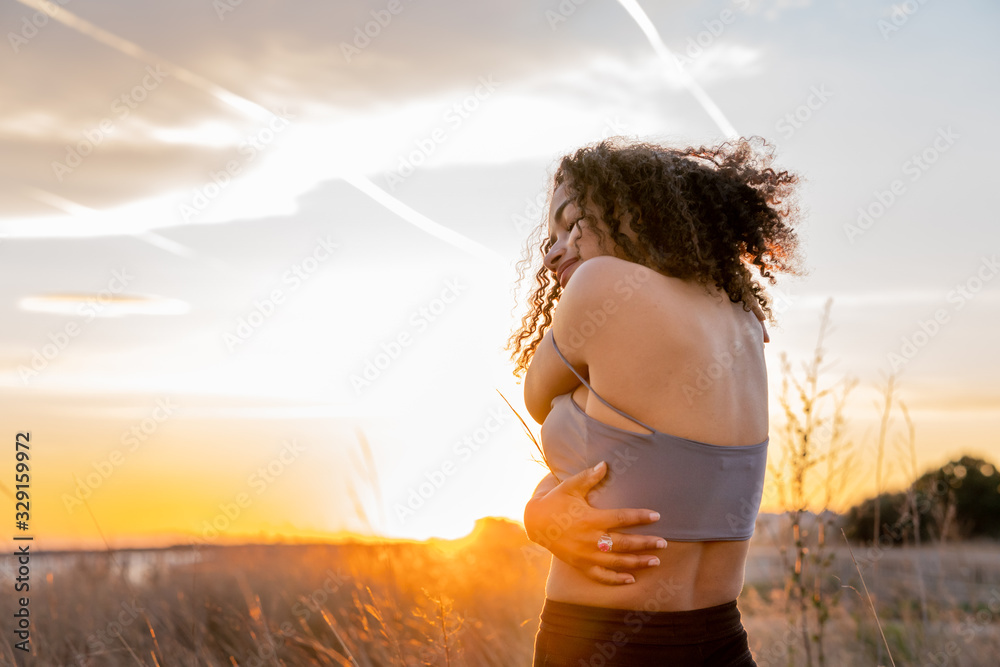 African American girl from the back hugging herself with the sky in the background - obrazy, fototapety, plakaty 