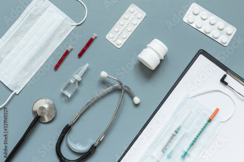 Medical flat lay. Phonendoscope, pills, syringe, ampoules for the treatment and diagnosis of disease and coronavirus virus on a gray background.