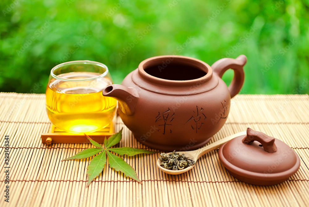Chinese tea ceremony in the garden with dry green tea in spoon on a bamboo table. Chinese tea ceremony in the garden with dry green tea in spoon on a bamboo table.
