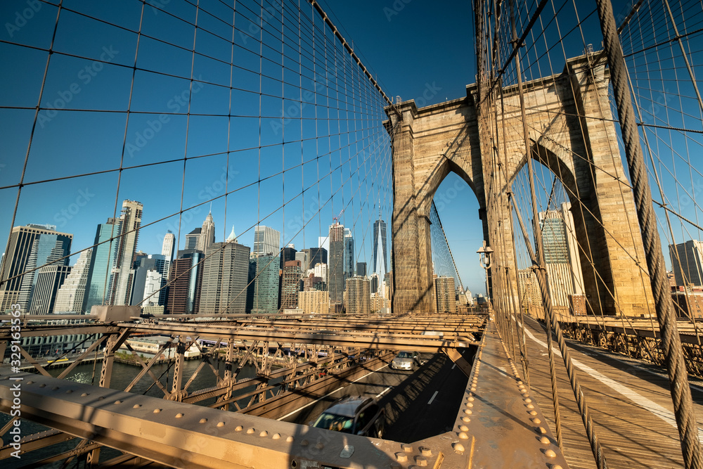 Fototapeta premium Early morning sun rises on the path of the Brooklyn Bridge over the East River connecting Manhattan New York to Brooklyn USA