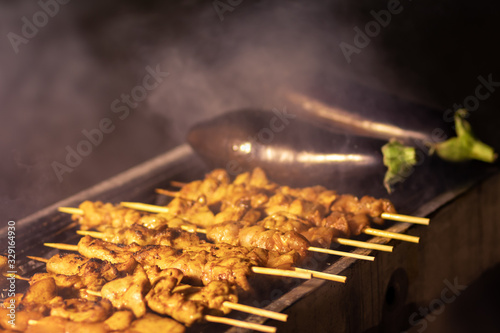 Chicken chunks skewers, grill, barbecue. On a metal bbq. In the grilling stages. Near roasted eggplant. Dark night background, kosher food. Lots of smoke photo