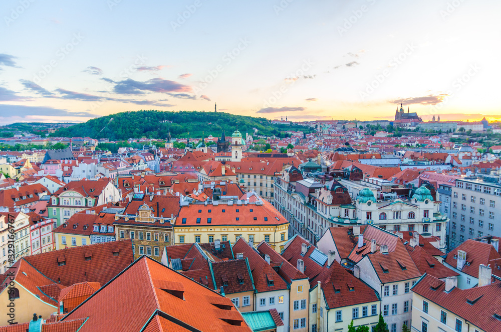 Top aerial panoramic view of Prague Old Town historical city centre with red tiled roof buildings and Prague Castle, St. Vitus Cathedral, Petrin hill garden in evening sunset, Czech Republic