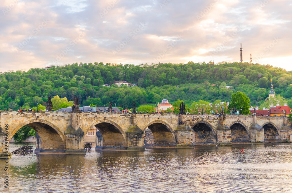 Fototapeta premium Charles Bridge Karluv Most with alley of dramatic baroque statues over Vltava river in Old Town of Prague historical center, garden on slope of Petrin Hill background, Czech Republic, Bohemia, Europe