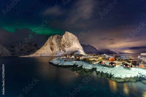 Beautiful Northern Lights in Hamnoy, Lofoten Island in Norway. Aurora Boreal over the small fishing village with its traditional red huts. Majestic green night sky.