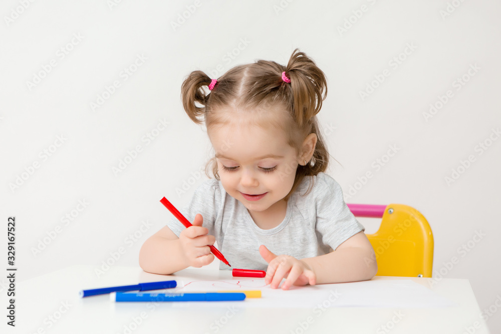 child a girl two years old sits at a table and draws on a white background child a girl two years old sits at a table and draws on a white background