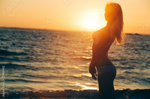 body a slim woman in swimsuit on sea  beach on sunrise. beautiful girl with long  hair enjoying sunset on sea shore . silhouette of sexy woman in underwear dream outdoors near river in summer morning  © mihail_pustovit
