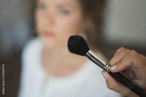 Close-up makeup brush on the background of the blurred face of the bride