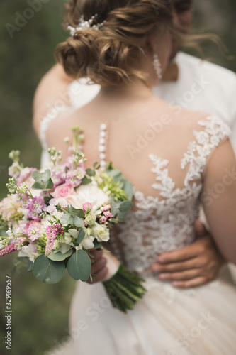 The groom in a white shirt with a bouquet of flowers in his hands embraces the bride.