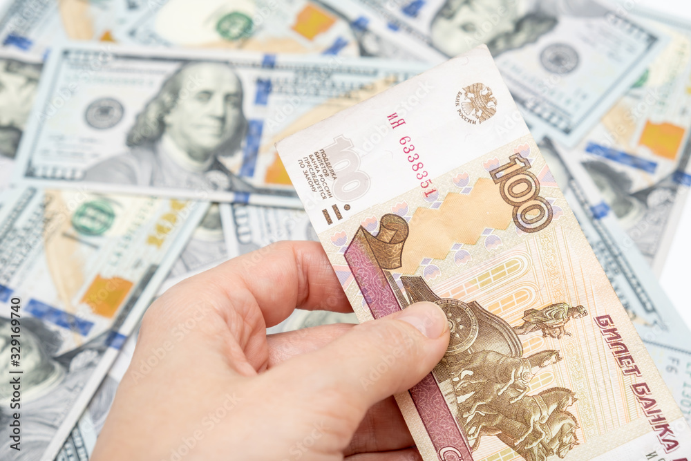 A hand holding one hundred ruble and american dollar banknotes on background, ruble devaluation and usd-rub exchange rate concept, hundred rubles for one dollar A hand holding one hundred ruble and american dollar banknotes on background, ruble devaluation and usd-rub exchange rate concept, hundred rubles for one dollar