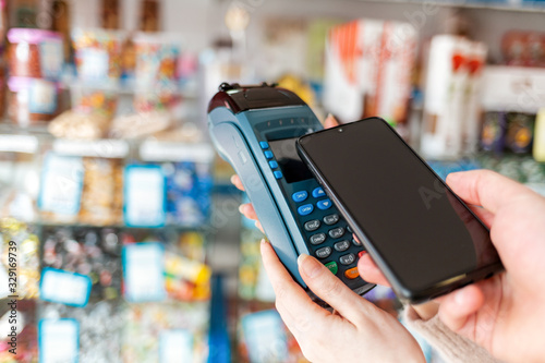 Women's hands are held by a payment terminal and a man pays for a purchase using a smartphone. Copy space. The concept of NFC, business and banking transactions