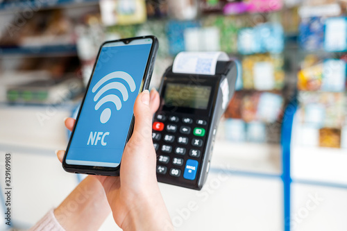 A woman's hands holds a payment terminal with a check and pays for a purchase using a smartphone.On the phone screen-wi-fi network.NFC concept, business and banking operations