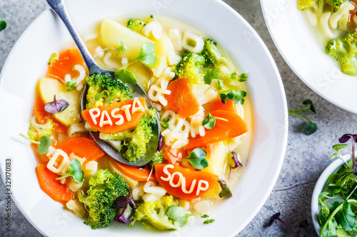 Healthy kids alphabet soup with broccoli, carrot and potato in white plate, top view.