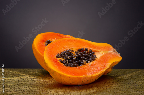 Bright vibrant orange papaya fruit sliced in half on a gold coloured surface with black seeds piling out photo