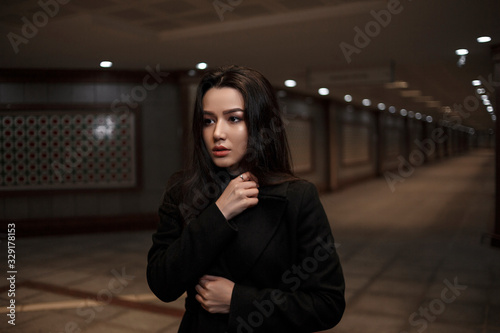 dramatic portrait of a beautiful young woman in a black coat in an underground passage.mosaics on the walls are not someone's works of art.these are walls in an underground passage in Eastern style