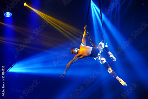 American strong sexy man do performance on aerial strap in blue lights. Sport training gym and lifestyle concept. Black background. 