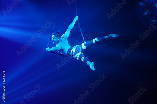 American strong sexy man do performance on aerial strap in blue lights. Sport training gym and lifestyle concept. Black background. 