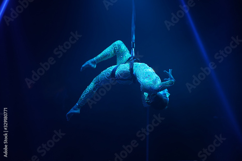 Flexible young woman make aerial performance , blue light, flexible split aerial circus show. Stretching women. Gymnast upside down