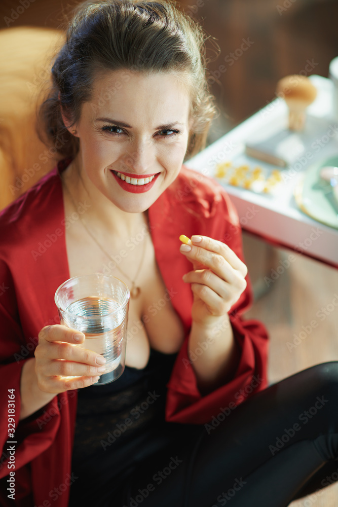 smiling trendy middle age woman with cup of water taking pill smiling trendy middle age woman with cup of water taking pill