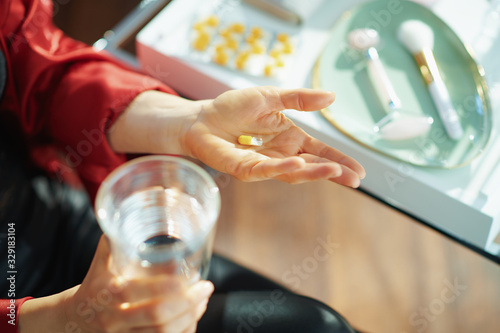 woman with cup of water taking pill near table with toiletries