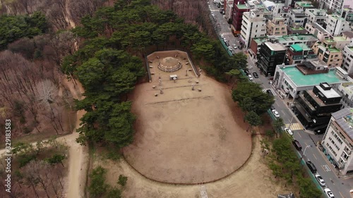 Seonjeongneung park tomb hill, surround with green trees, aerial shot. Gultural Heritage site at Gangnam district of Seoul. Residential buildings seen on right side outside park photo