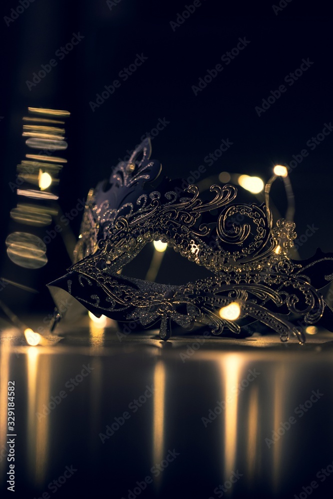 A portrait of a venetian mask full of mystery on a wooden table surrounded by lights and their reflection. It is perfect to hide someones identity. - obrazy, fototapety, plakaty 