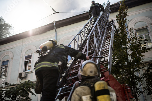 Wallpaper Mural Firefighters on ladders in oxygen masks extinguish the fire in an old house in the middle of the city Torontodigital.ca