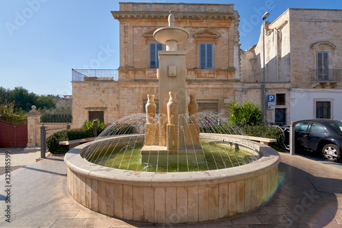 Fountain In Bright Sunshine With Typical Italian Building In The Backgroudn At Alberobello Bari Province Apulia Italy