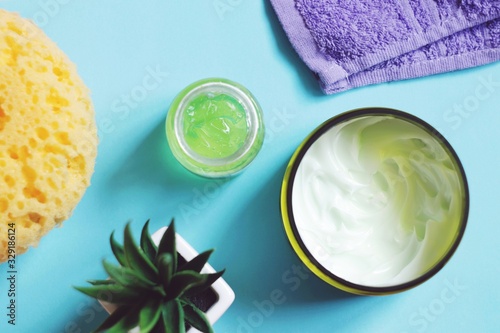 Yellow sponge, moisturizing face cream, natural aloe gel and purple towel. Flat lay beauty photography