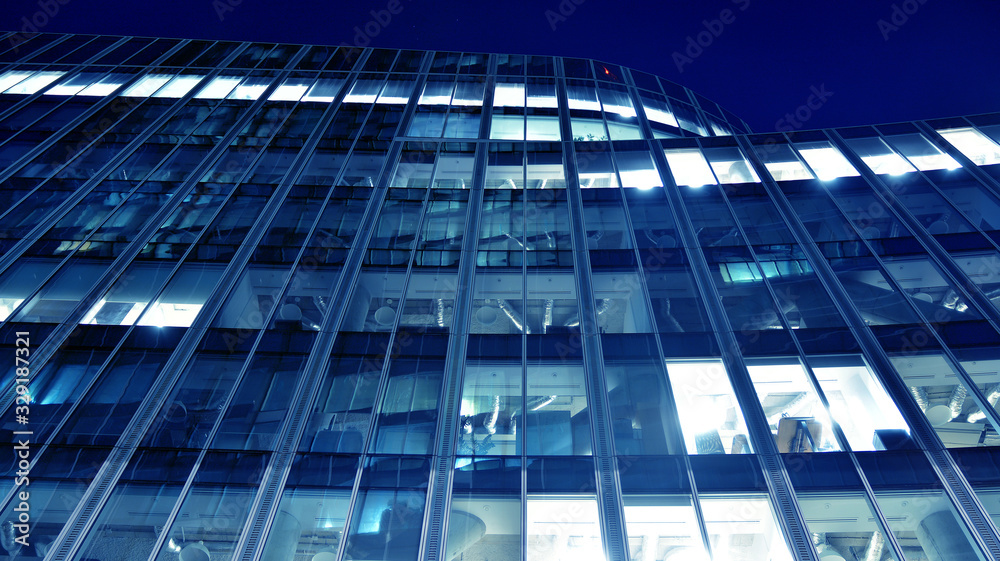Night architecture - building with glass facade.Blue color of night lights. Modern building in business district. Concept of economics, financial. Photo of commercial office building exterior. Abstra Night architecture - building with glass facade.Blue color of night lights. Modern building in business district. Concept of economics, financial. Photo of commercial office building exterior. Abstra