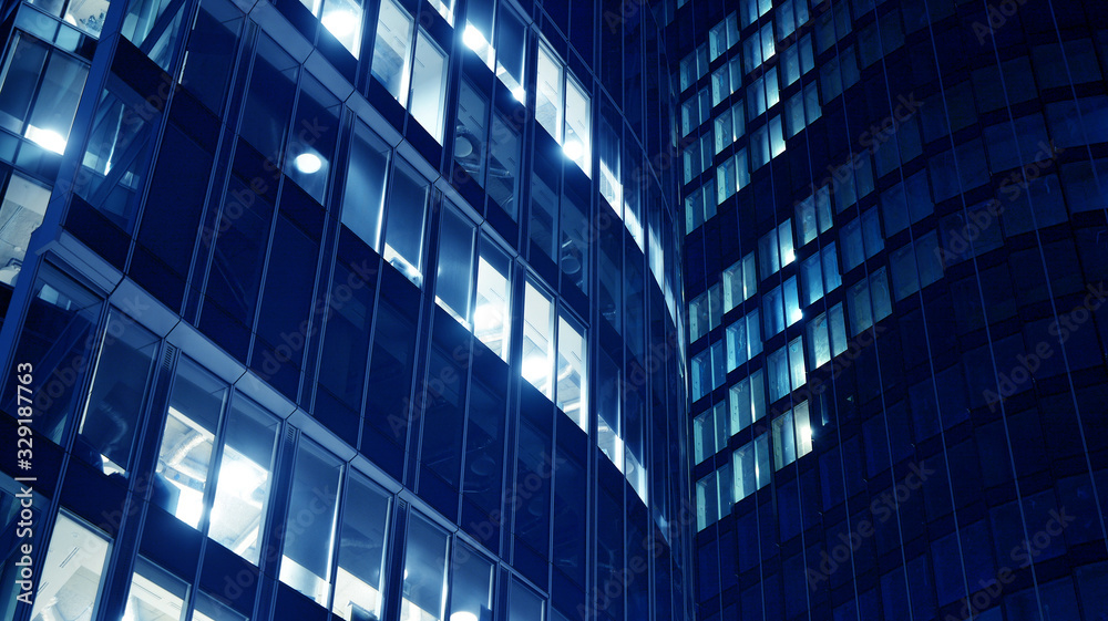 Night architecture - building with glass facade.Blue color of night lights. Modern building in  business district. Concept of economics, financial. Photo of commercial office building exterior. Abstra