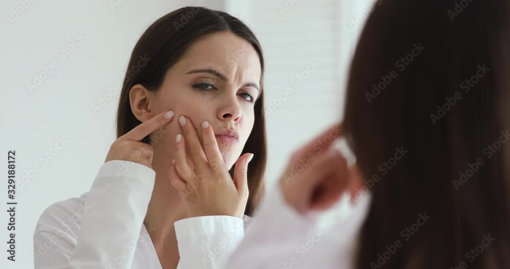 Upset teen girl feeling worried about facial skin problem looking in mirror. Depressed young woman touching face frustrated by blackheads, acne and pimples. Blemish skincare beauty treatment concept Upset teen girl feeling worried about facial skin problem looking in mirror. Depressed young woman touching face frustrated by blackheads, acne and pimples. Blemish skincare beauty treatment concept