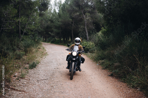 Man drives touring adventure motorcycle on beautiful scenic forest road. Motorcyclist or biker rides on gravel dirt road during summer tour or travel. Touring adventure motorcycle