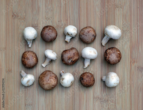 Arrangement of raw white champignons and brown crimini mushrooms on a bamboo board